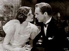 Hepburn and a young man acting in A Bill of Divorcement. They are holding hands and looking at each other emotionally.