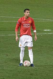 Cristiano Ronaldo - wearing a long-sleeved red jersey, white shorts with a number 7 on the left-leg side and a white armband on the left arm - prepares to take a free kick.
