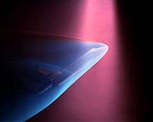 A violet beam from above produces a blue glow about a Space shuttle model
